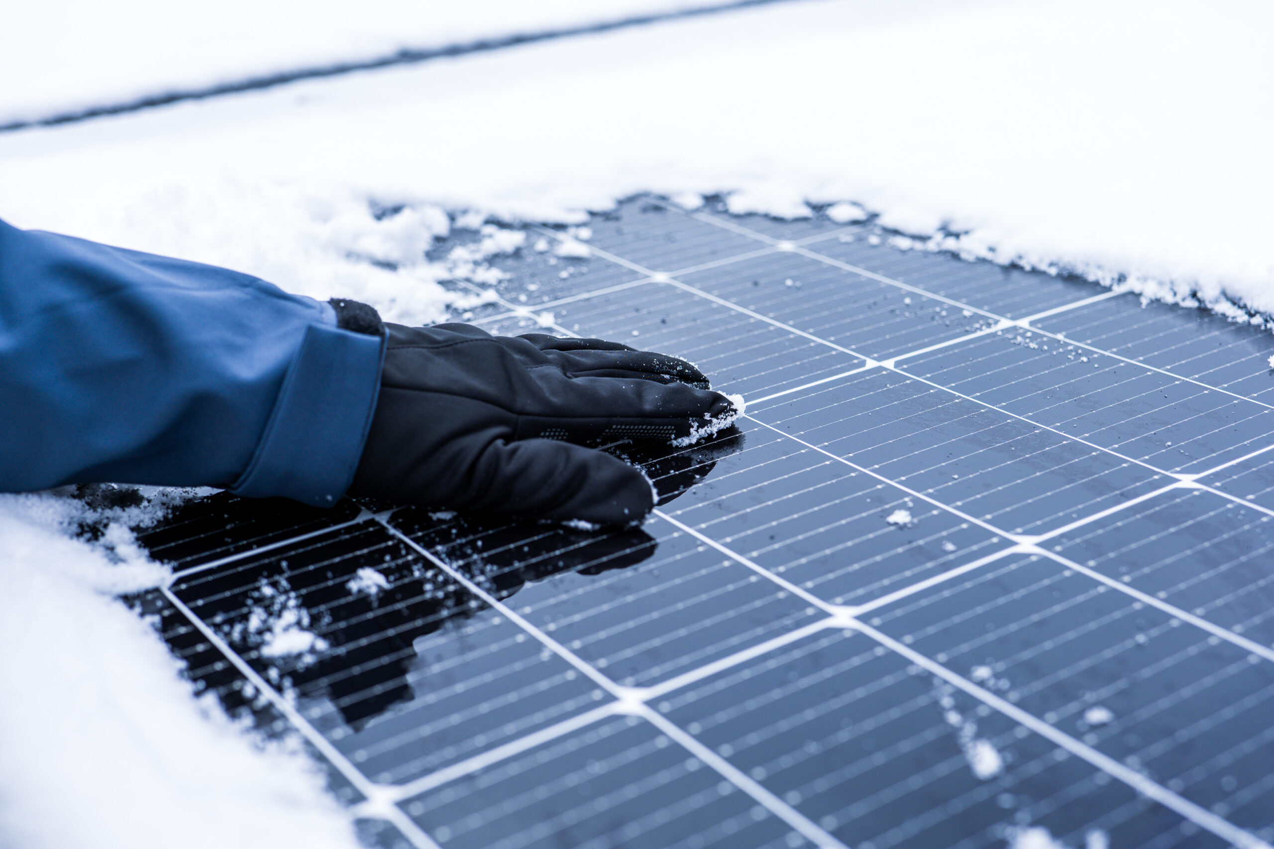 a hand wiping snow off a solar panel in winter installed by solar pros