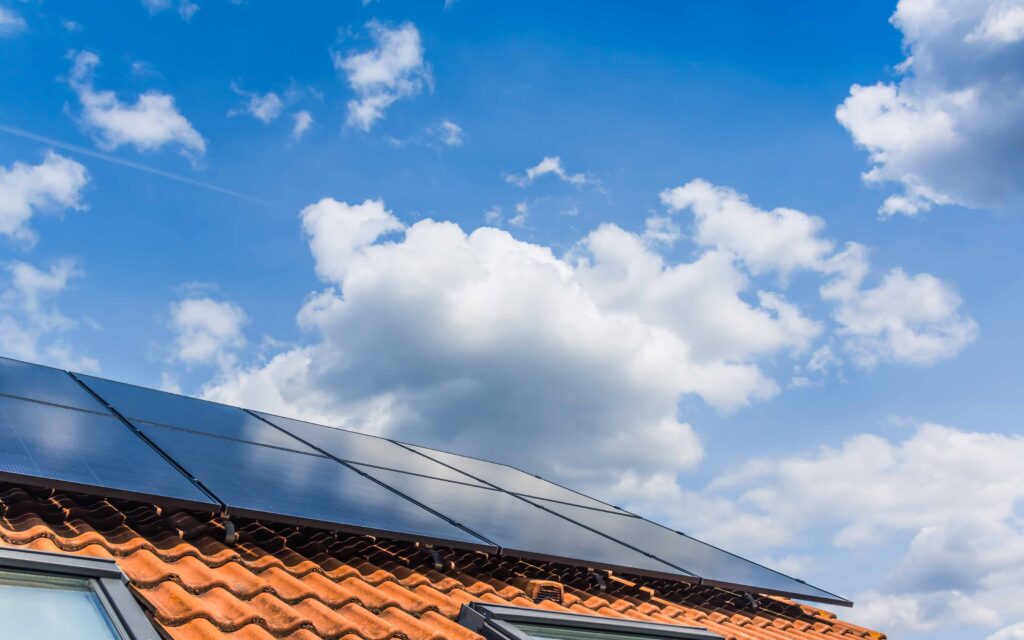 Red-tiled house roof with solar panels under a blue sky with scattered clouds